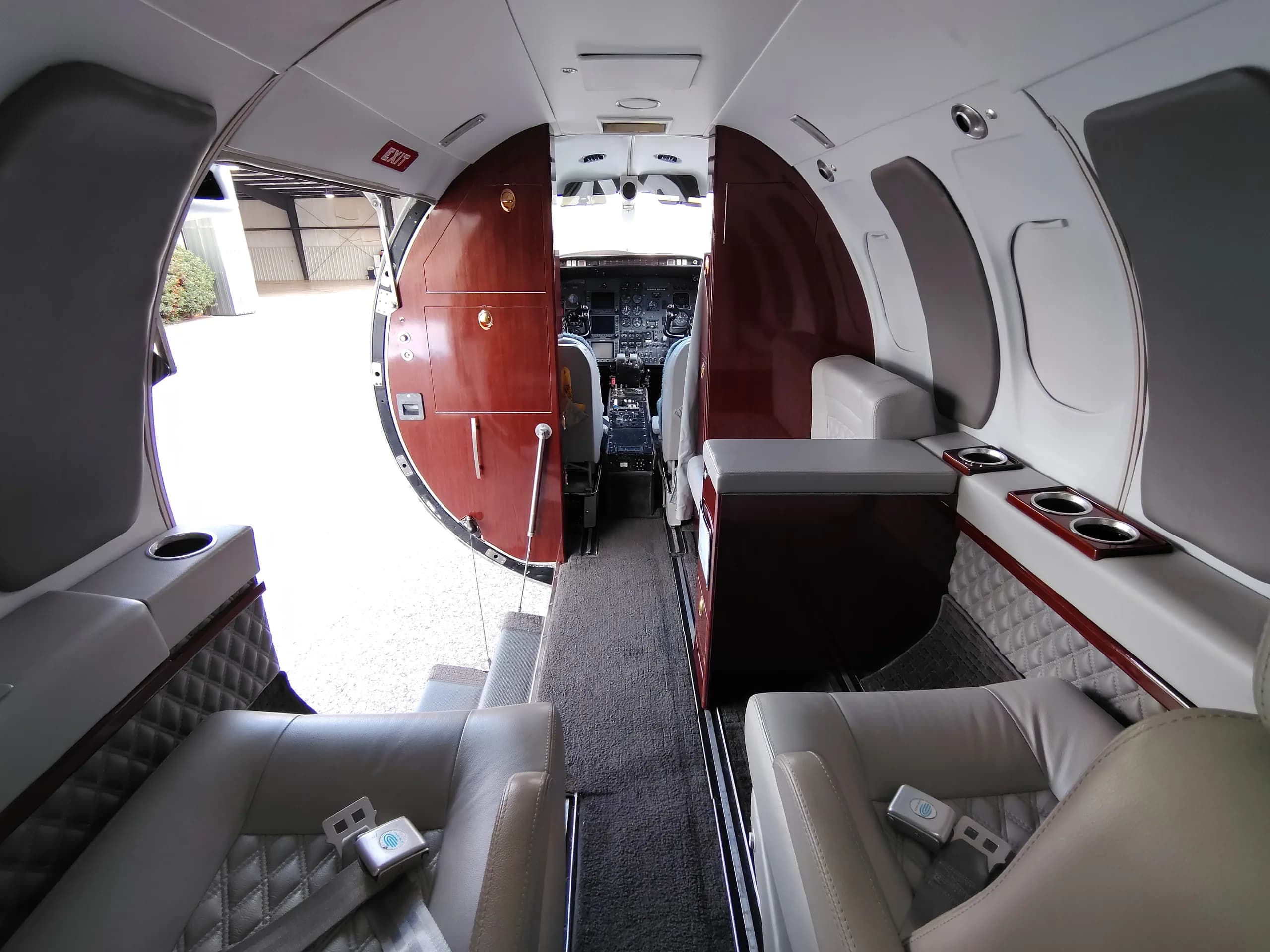 View from the aircraft cabin looking forward into the open cockpit, showing light gray seats and wood paneling.