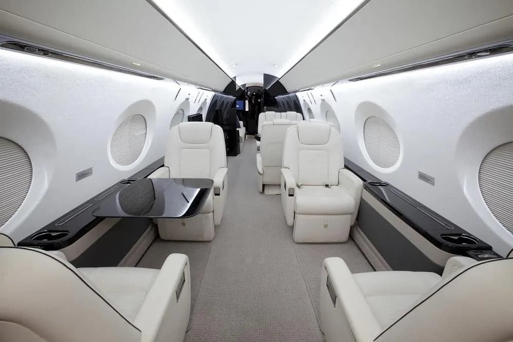The interior cabin of a business jet showing cream leather seats and a deployed dark table.