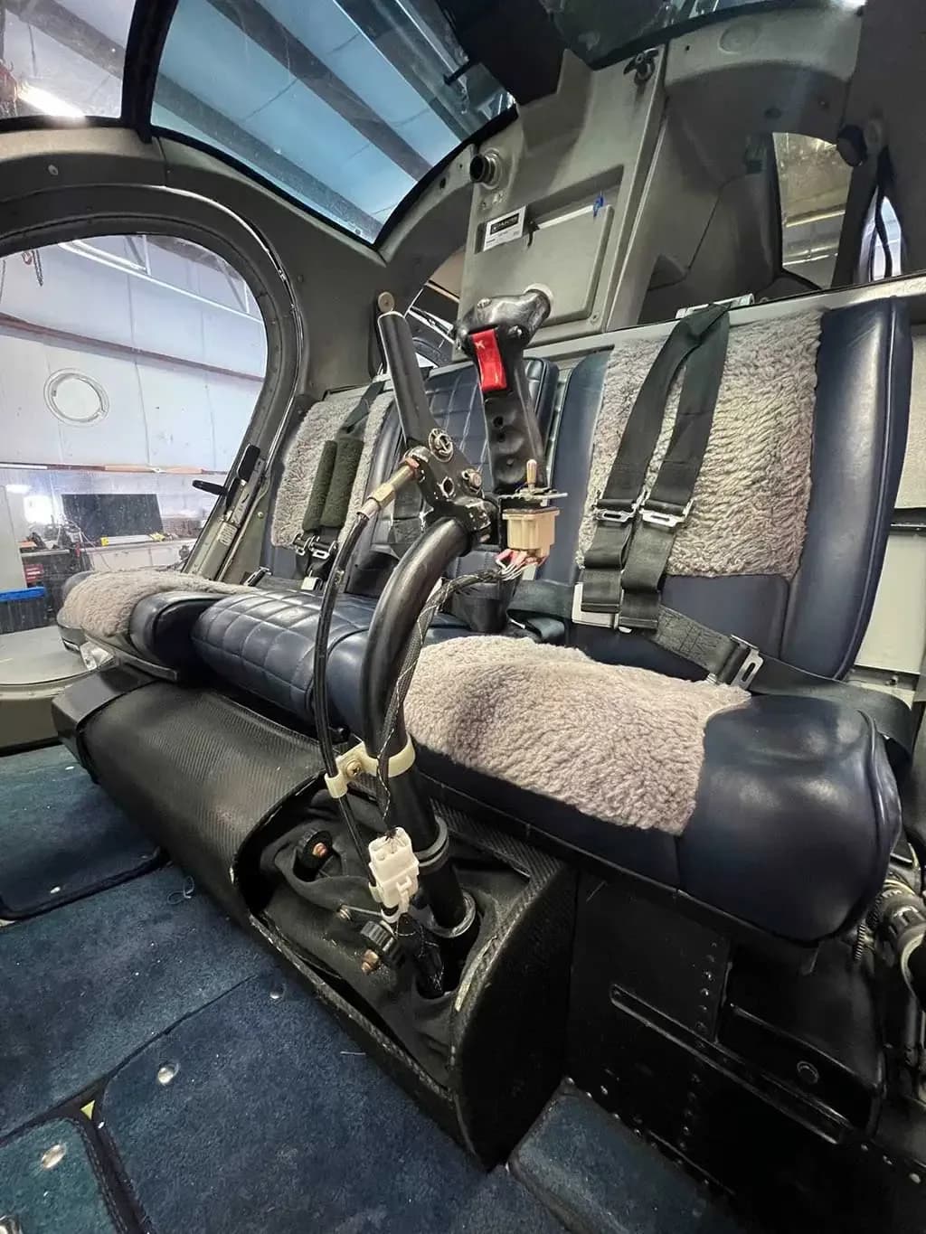 The interior of the helicopter cabin, showing blue seats with sheepskin covers and flight controls.