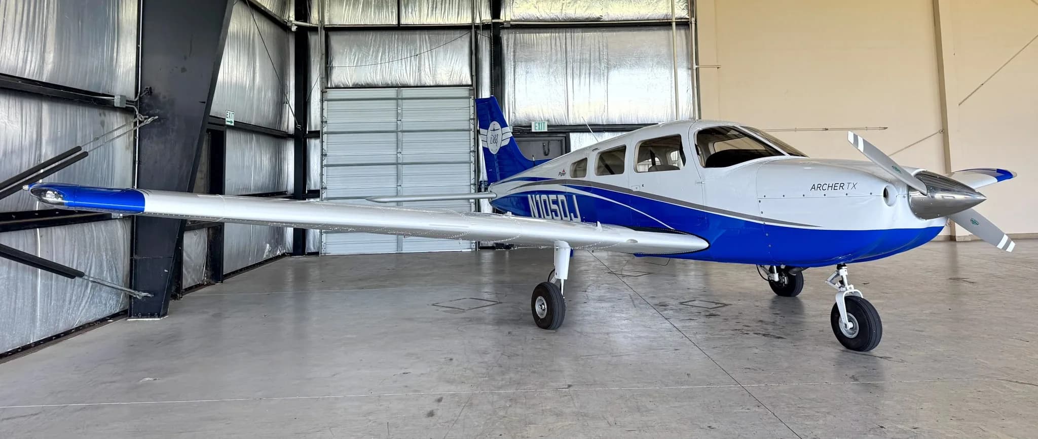 The white and blue Piper Archer TX aircraft, N105DJ, is seen from the front-right in a hangar.