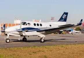 A white twin-engine turboprop aircraft with blue stripes and a 'GT' logo on the tail, parked on an airport tarmac.