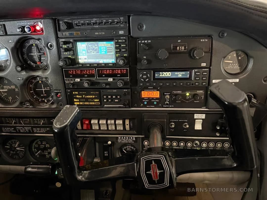 A detailed view of an aircraft cockpit's instrument panel, showing various gauges, radios, and a control yoke with an Oldsmobile-like logo.