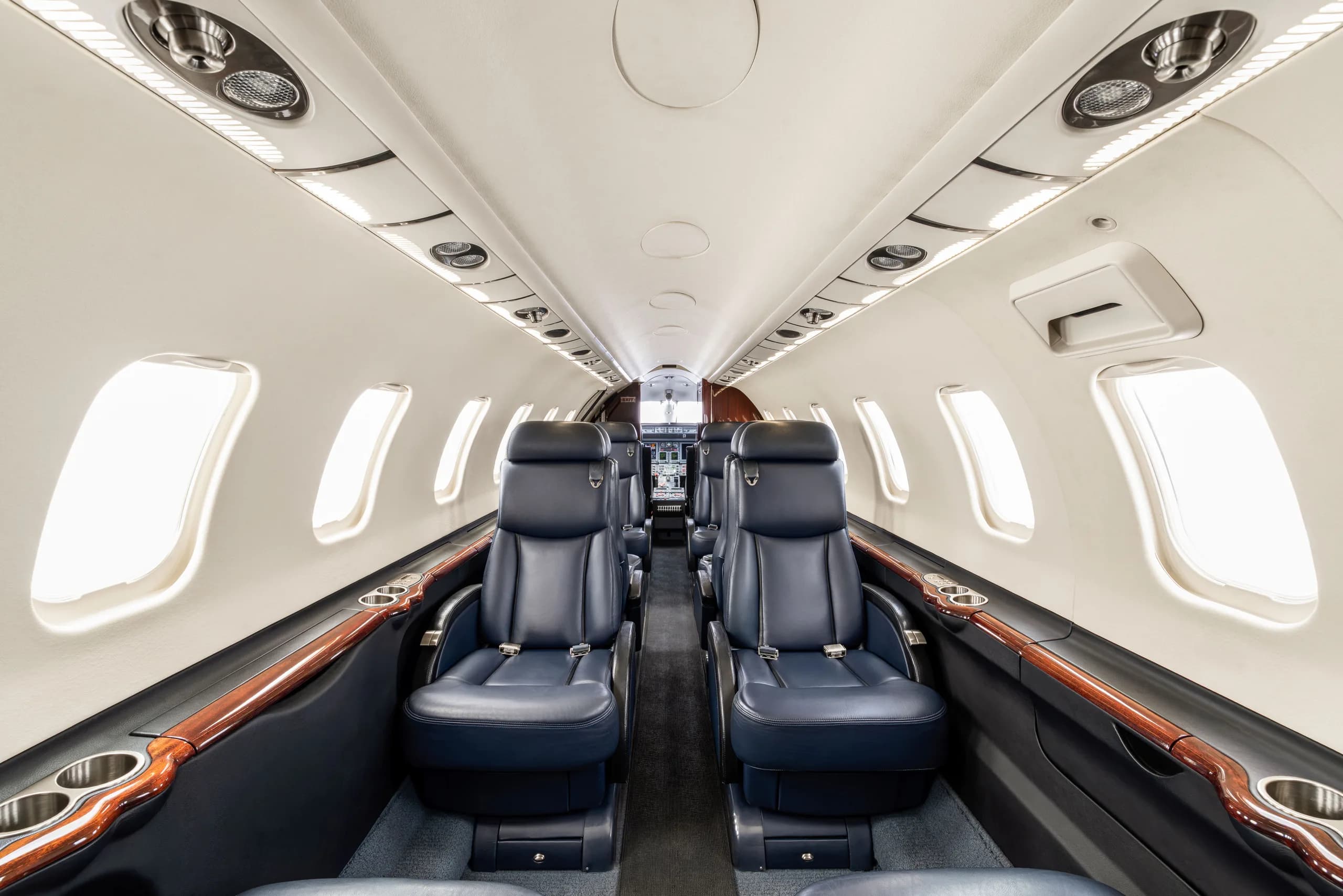 The interior cabin of a private jet, featuring dark blue leather seats and light-colored walls with wood trim.