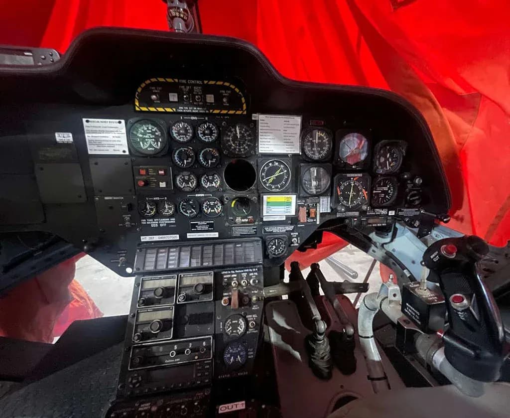 A close-up view of a helicopter's instrument panel with various gauges, switches, and flight controls.