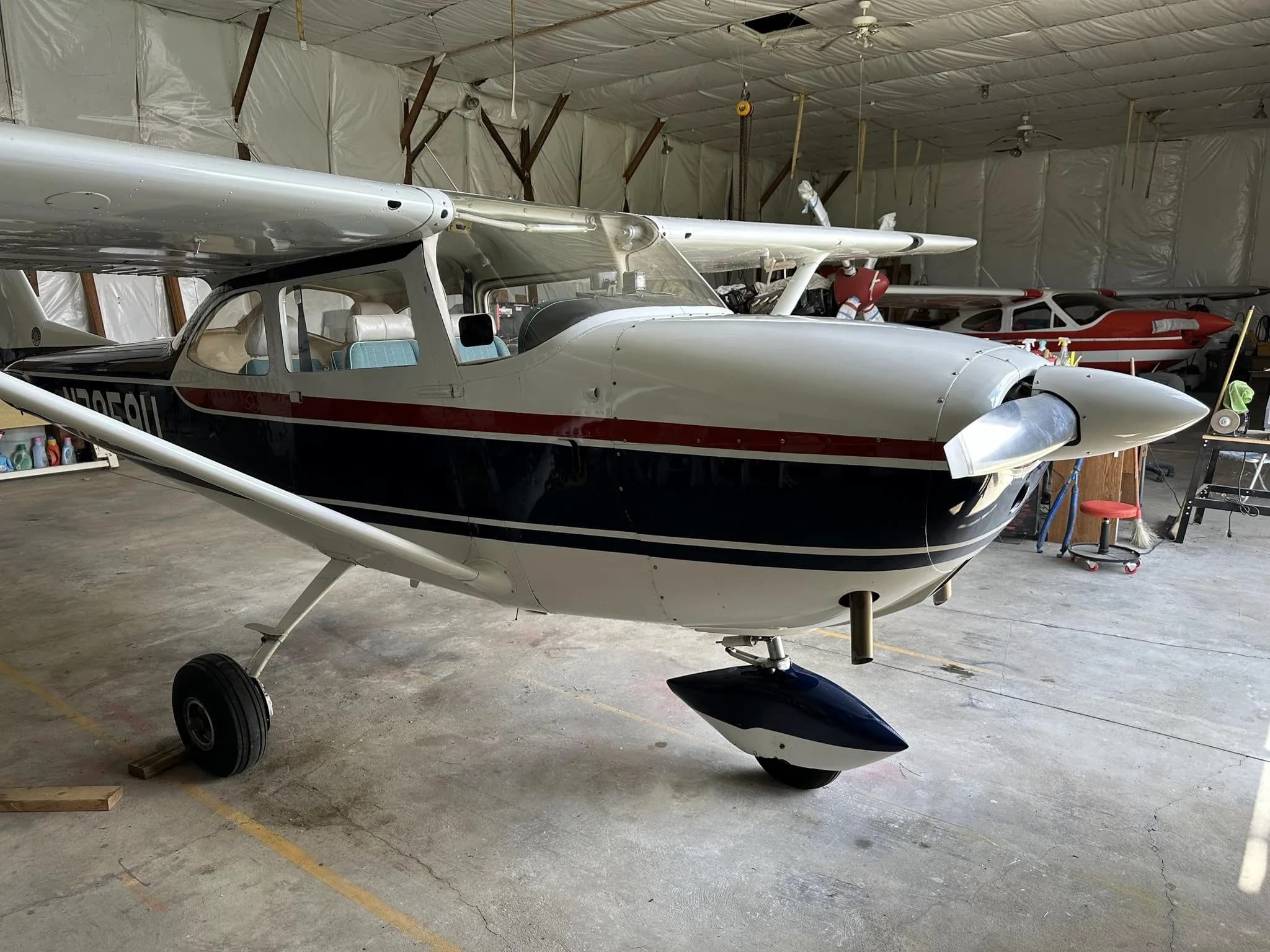 A front-quarter view of the white and blue Cessna N7959U with a red stripe in a hangar.
