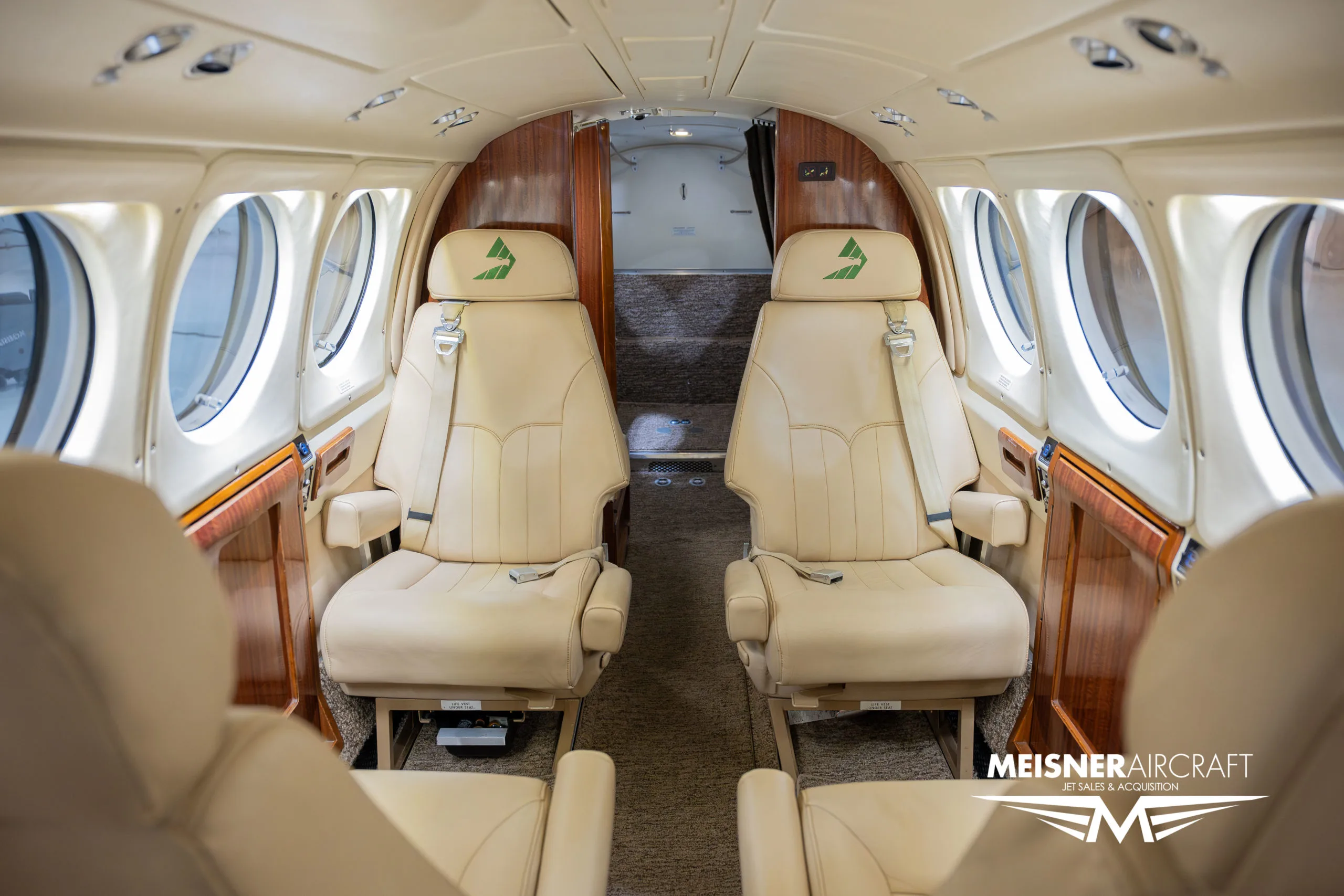 The interior cabin of an aircraft with beige leather seats and wood accents, looking towards the rear.