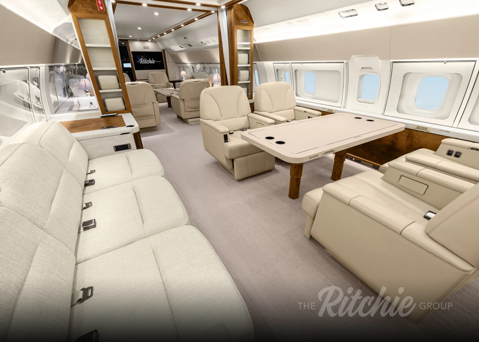 A spacious aircraft cabin with light-colored seating, a dining table, and large windows.