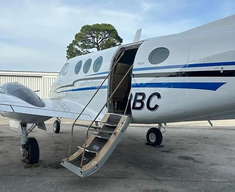 A close-up view of the open airstair door and fuselage of a white Beechcraft King Air with blue stripes, showing the registration N82BC.