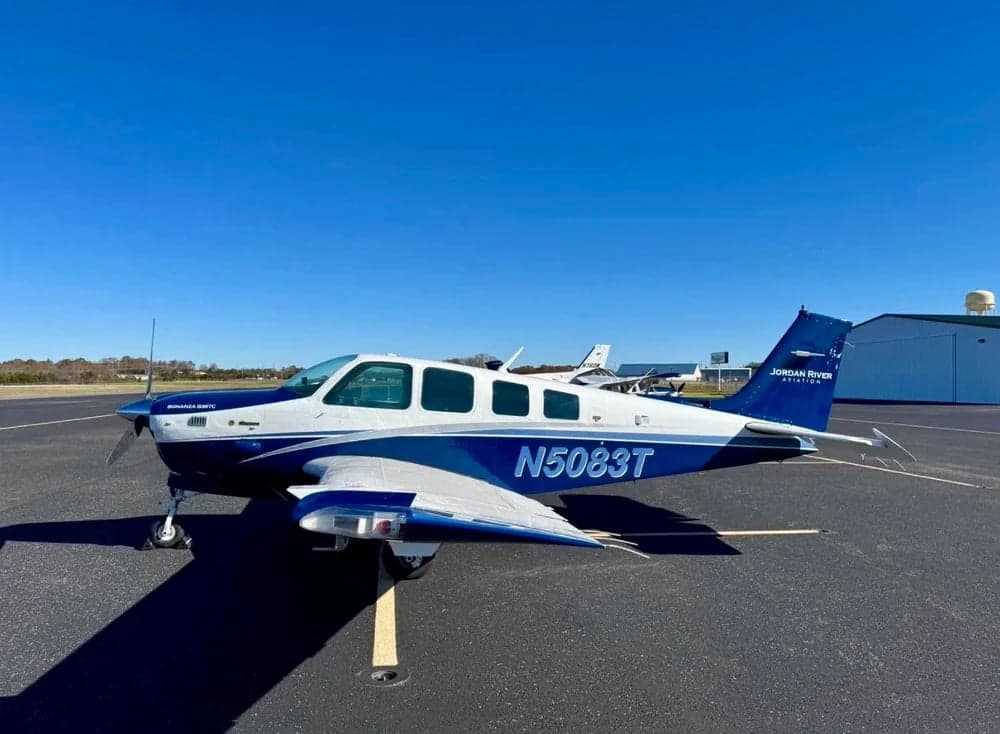A blue and white Mooney M20J aircraft with tail number N5083T is parked on the tarmac.