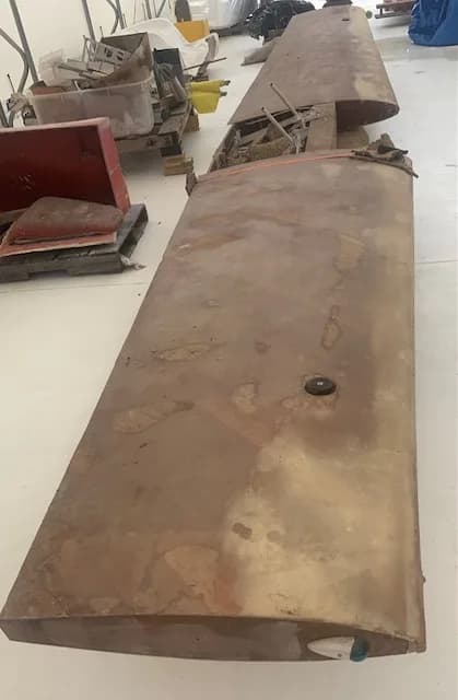 A detached, weathered aircraft wing lying on the floor in a workshop.