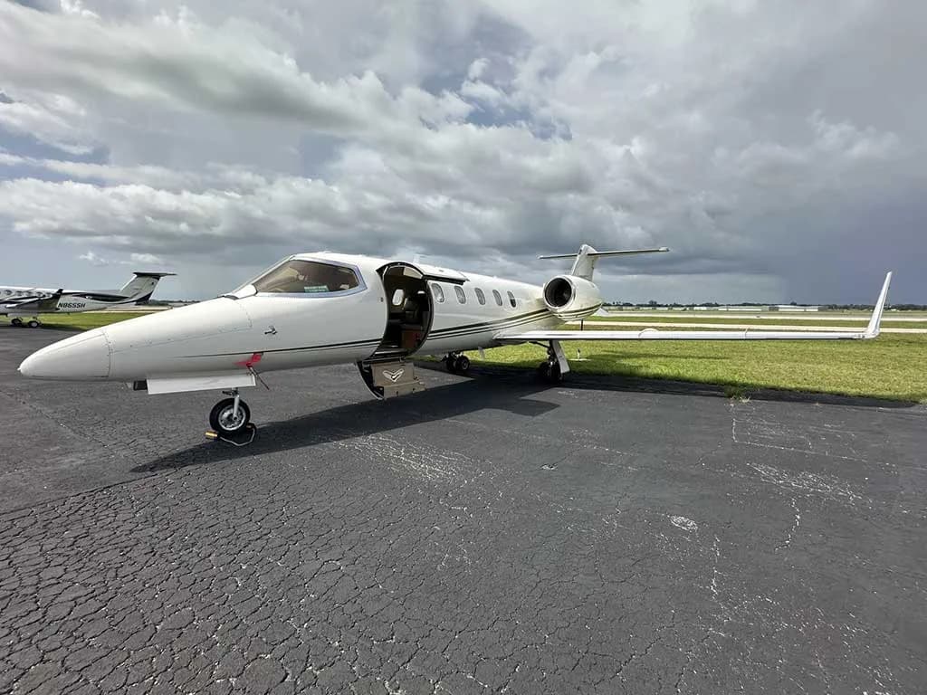A white Learjet 35A with its main entry door open, parked on an asphalt ramp under a cloudy sky.