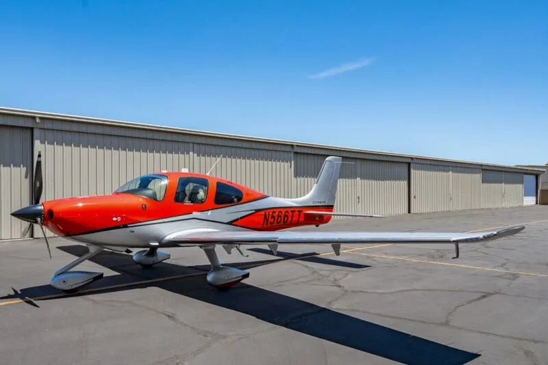 Three-quarter front view of a red and silver Cirrus SR22T aircraft (N566TT) parked on an airfield.