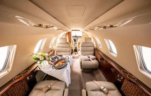 The luxurious interior cabin of a private jet, featuring beige leather seats and a table set with food and flowers.