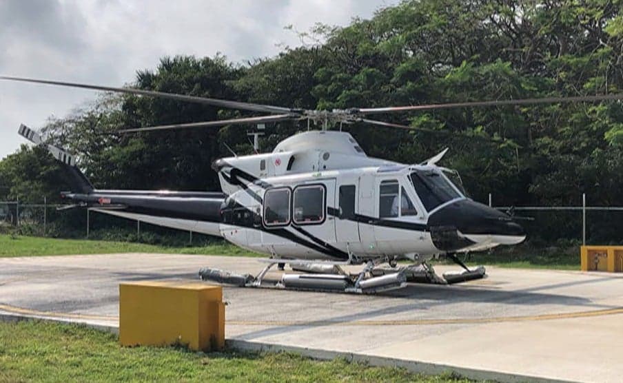 A white and black helicopter is parked on a helipad surrounded by trees.