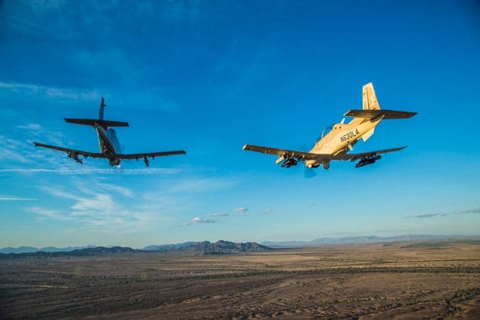 Two AT-6 light attack aircraft flying over a desert landscape.