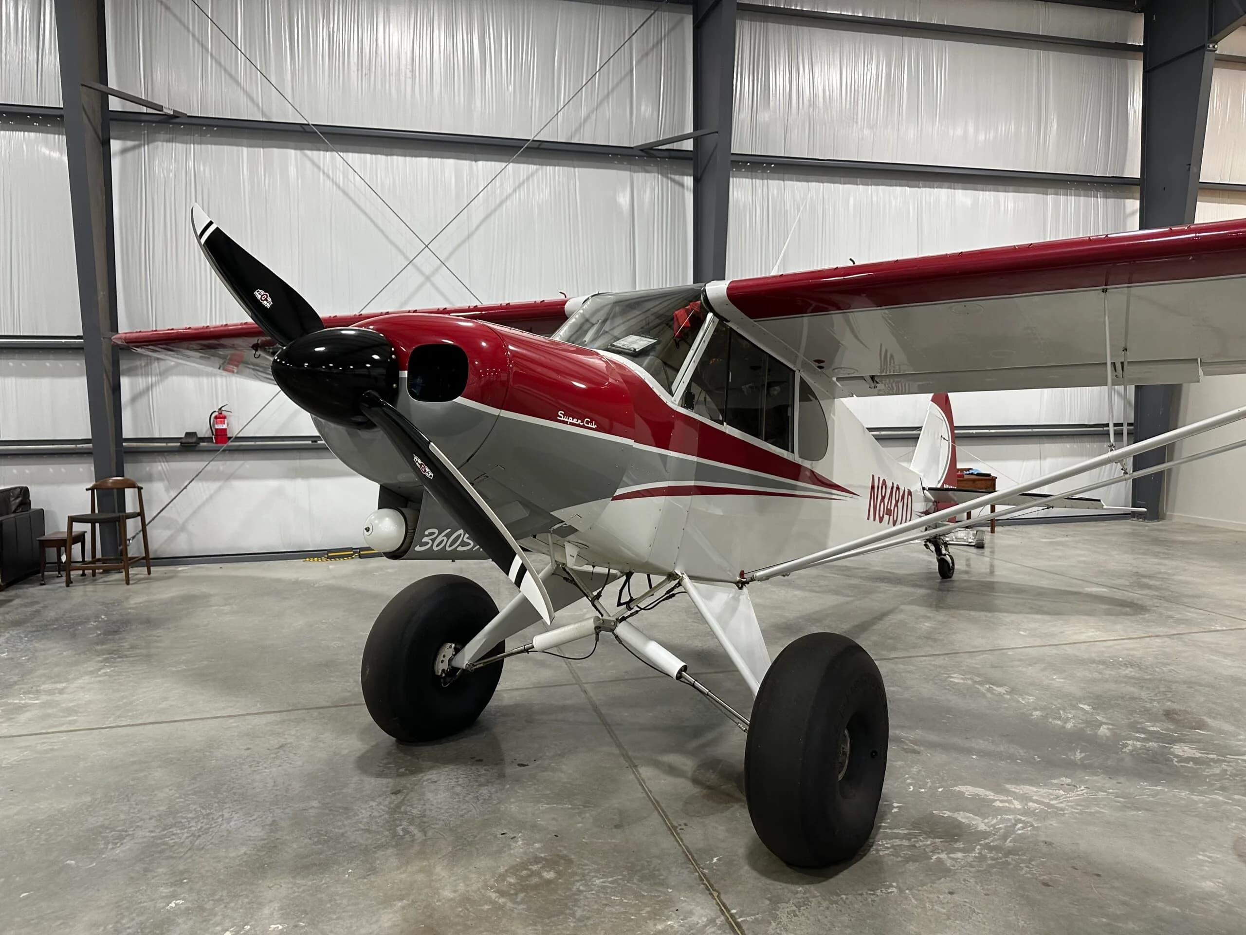 A red, white, and grey Super Cub aircraft with large tundra tires is parked inside a hangar.