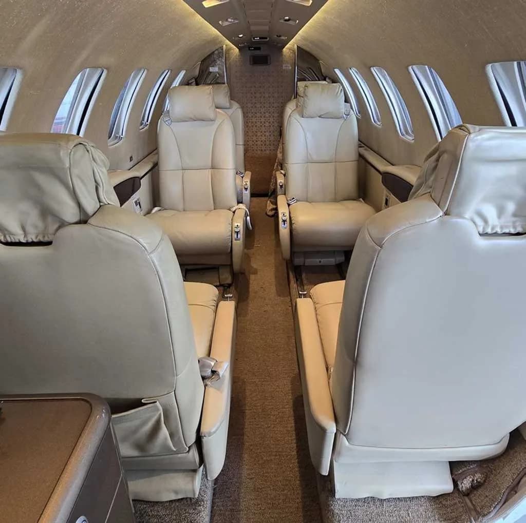 Interior view of a private jet cabin with light beige leather seats and a central aisle.