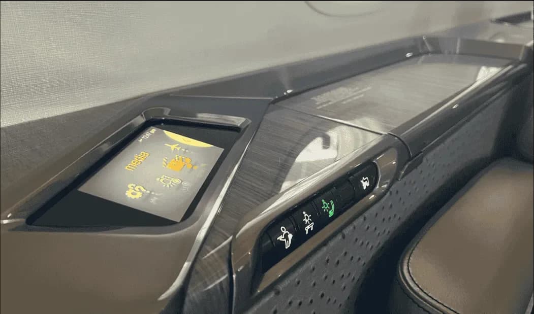 A close-up of an aircraft cabin control panel with a digital display showing "media" and various function icons.