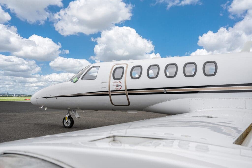 A close-up view of the front fuselage of a white Cessna Citation CJ3 (D-IALI) private jet, showing the cockpit windows and passenger door.