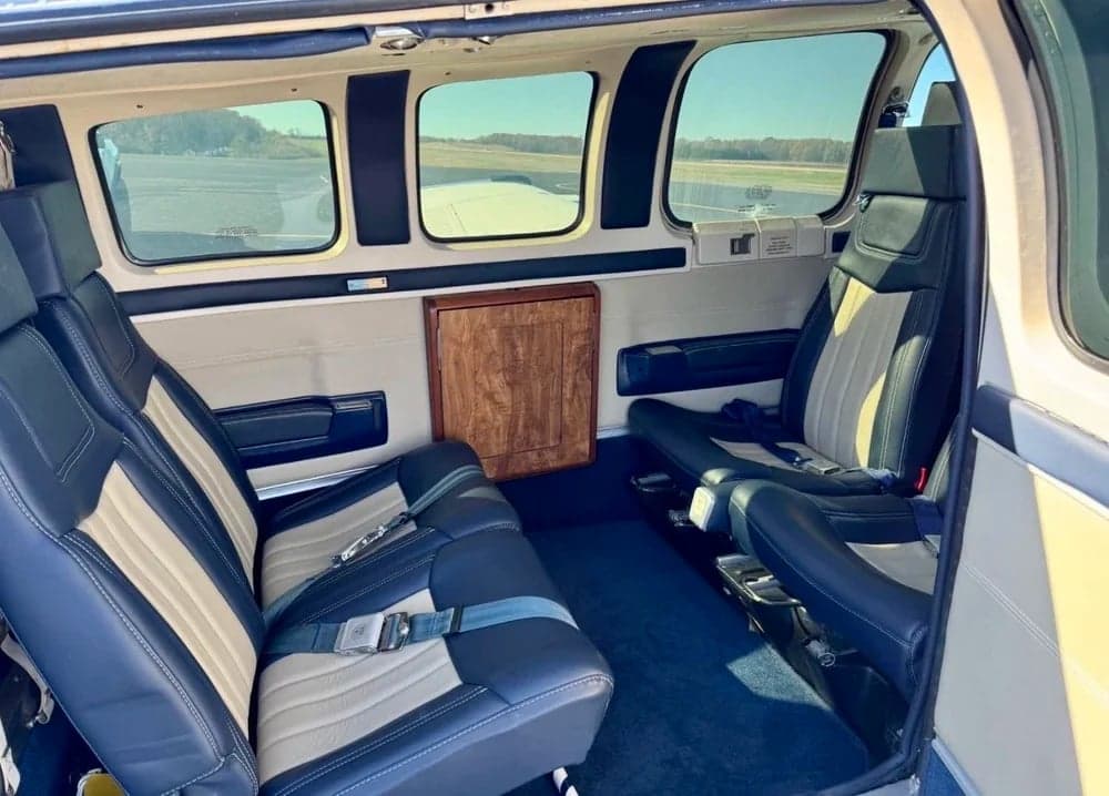 The interior of the aircraft features blue and beige leather seats and a wooden cabinet.
