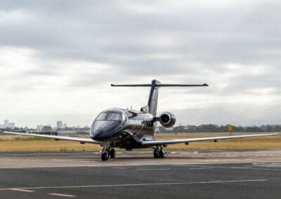 Front view of a black Pilatus PC-24 jet on the tarmac with a cloudy sky.