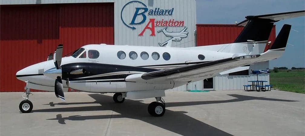 King Air with white and black paint scheme parked in front of a hangar.