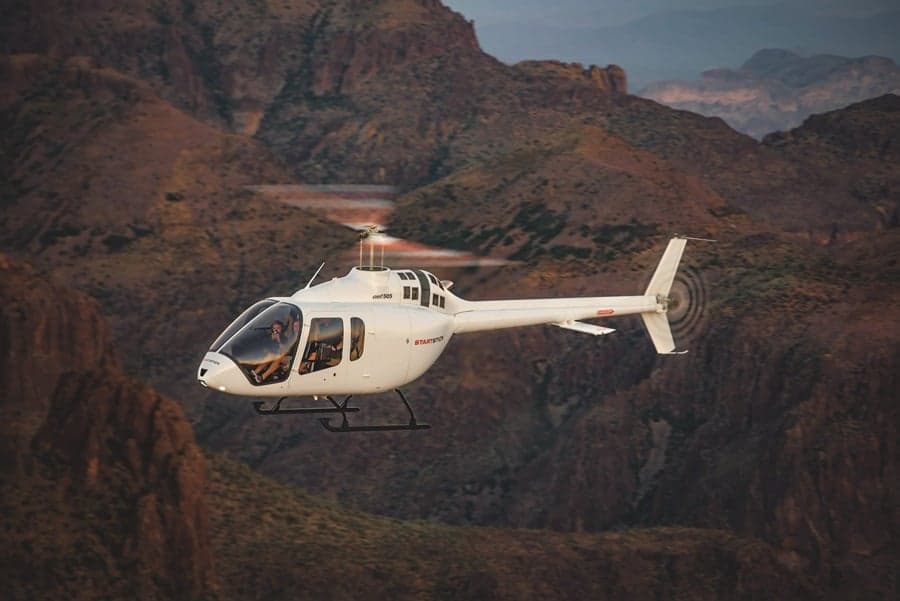 A white helicopter flying in front of a mountain range.
