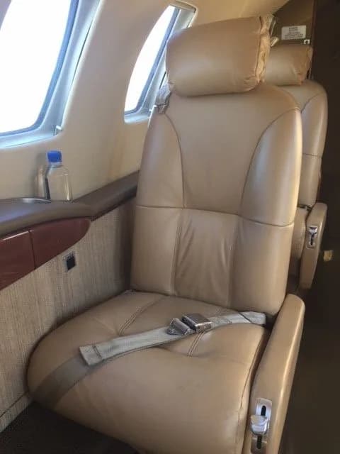 Aircraft interior with a tan leather seat and a bottle of water on the side table.