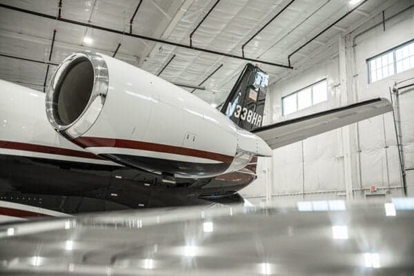 The tail and engine of a Citation jet, N338HR, are visible in a hangar.
