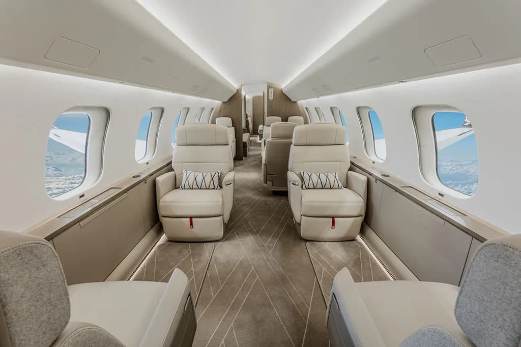 The luxurious interior of a business jet cabin with beige leather seats and patterned pillows.