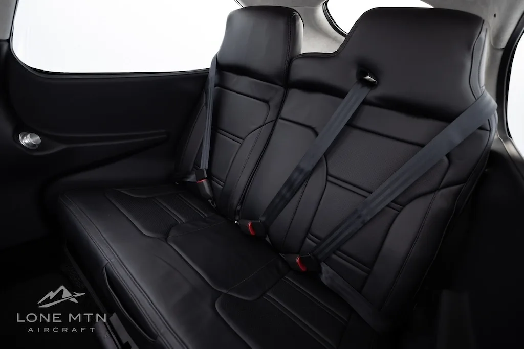 A close-up view of the black leather rear seats with seatbelts in the aircraft cabin.