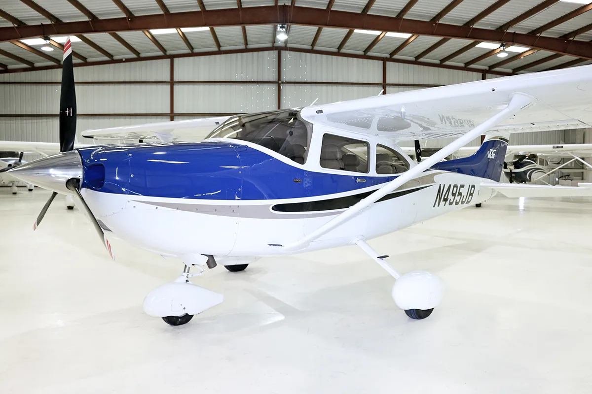 A front-side view of a white and blue single-engine propeller aircraft, N495JB, parked in a hangar.