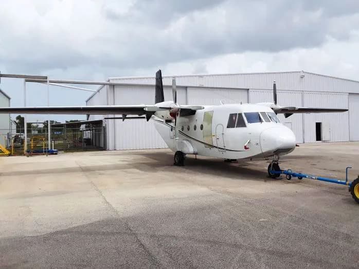 A white Shorts Skyvan aircraft parked in front of a hangar.
