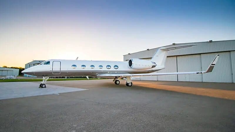 A Gulfstream jet parked on the tarmac in front of a hangar.