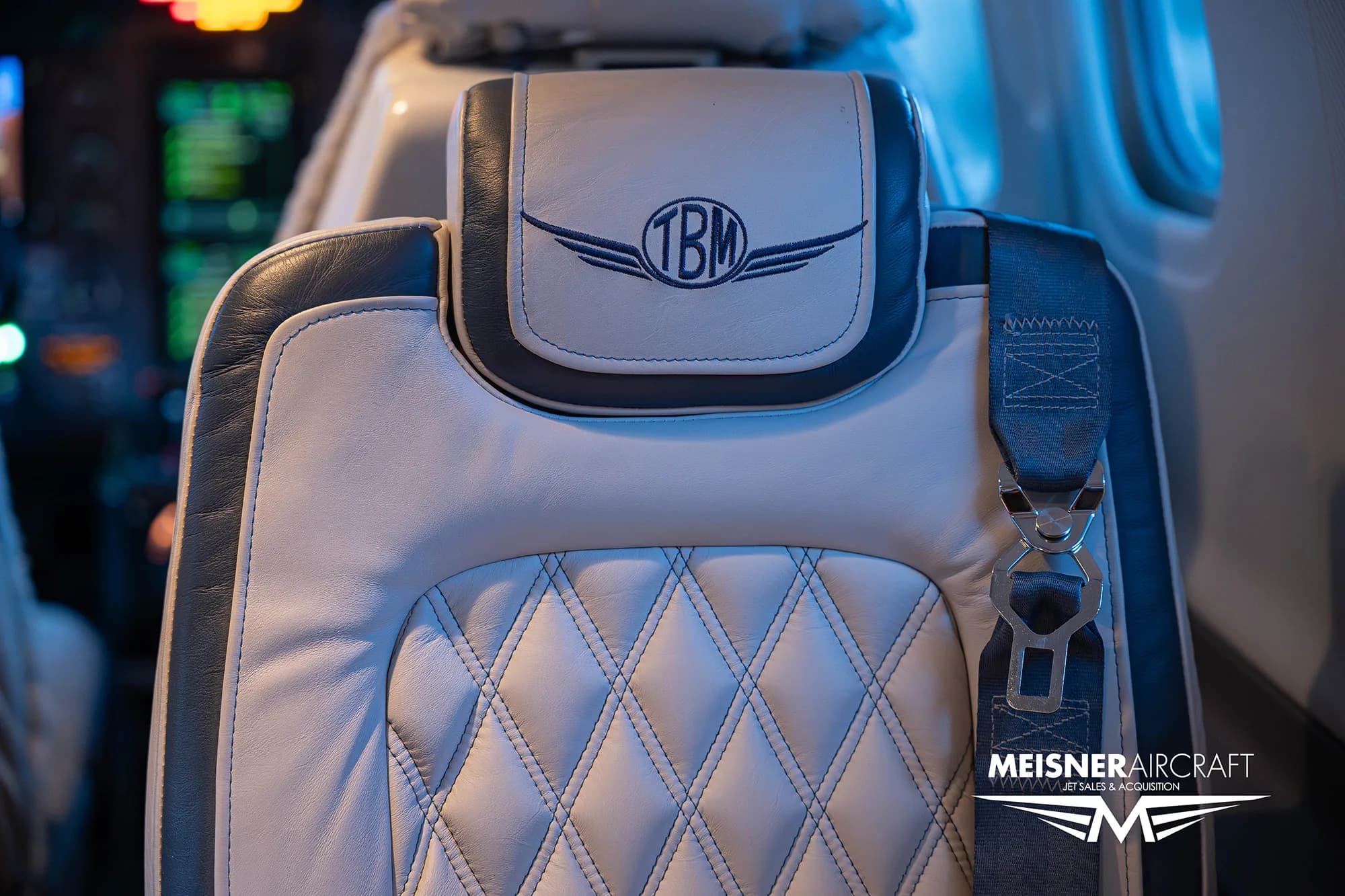 A close-up of a quilted leather aircraft seat headrest with the 'TBM' logo embroidered.