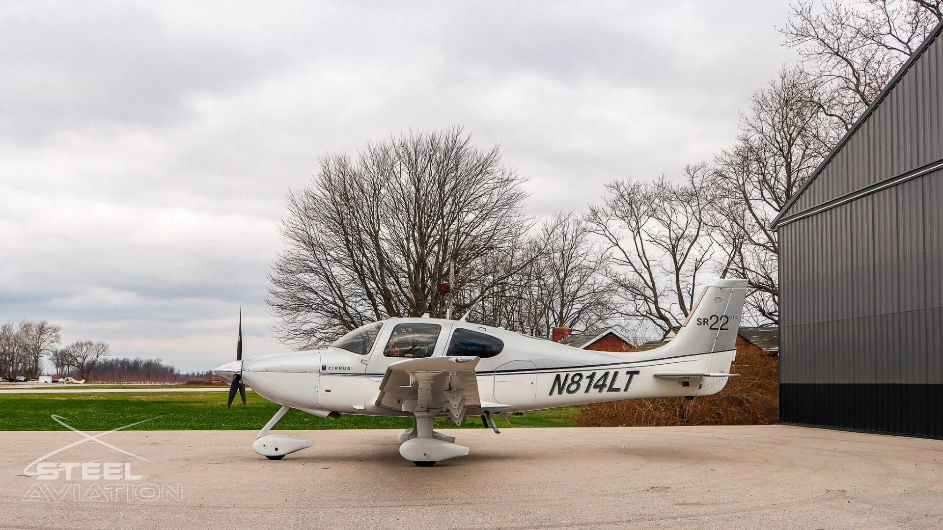 A side view of the white and silver Cirrus SR22 aircraft (N814LT) with its flaps extended, parked on an apron.