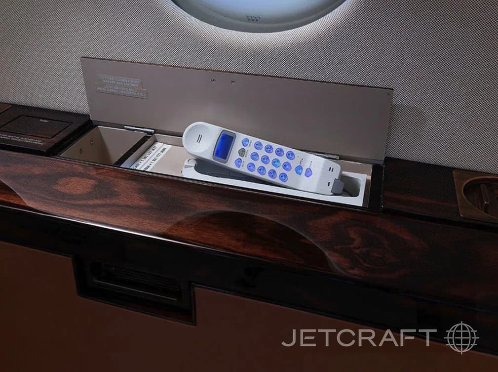A white cordless phone with blue illuminated buttons stored in a compartment within a dark wood panel.