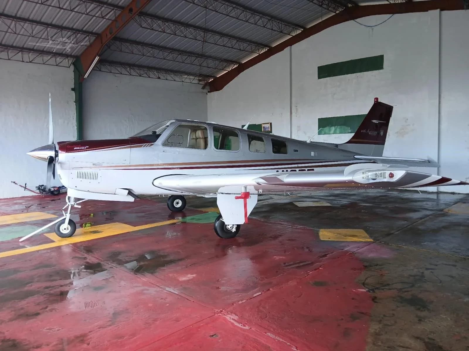A Beechcraft Bonanza in a hangar with a silver and maroon paint scheme.
