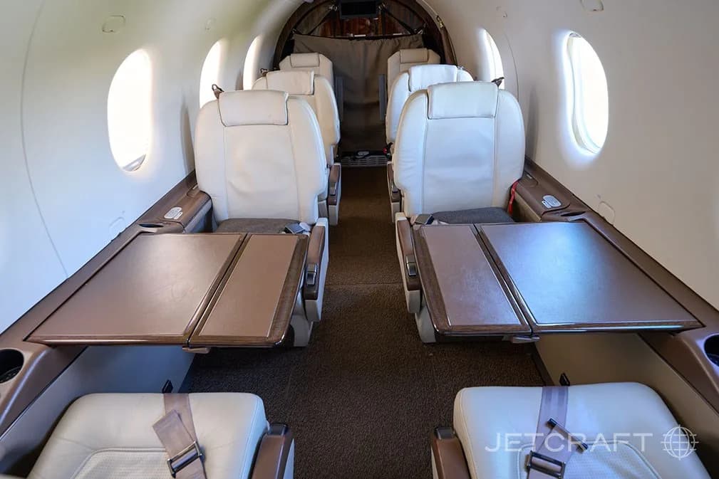 The aircraft cabin interior with light cream leather seats and brown fold-out tables.