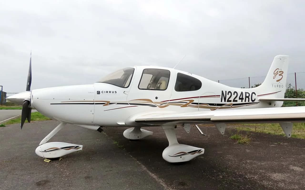 A white Cirrus SR22T (N224RC) with brown and black stripes parked on an asphalt surface under an overcast sky.