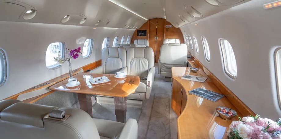 A wide view of a private jet's luxurious cabin, showcasing a dining area with a wooden table and multiple leather seats.
