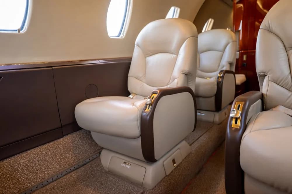 A close-up view of the beige leather passenger seats with brown accents inside a private jet cabin.
