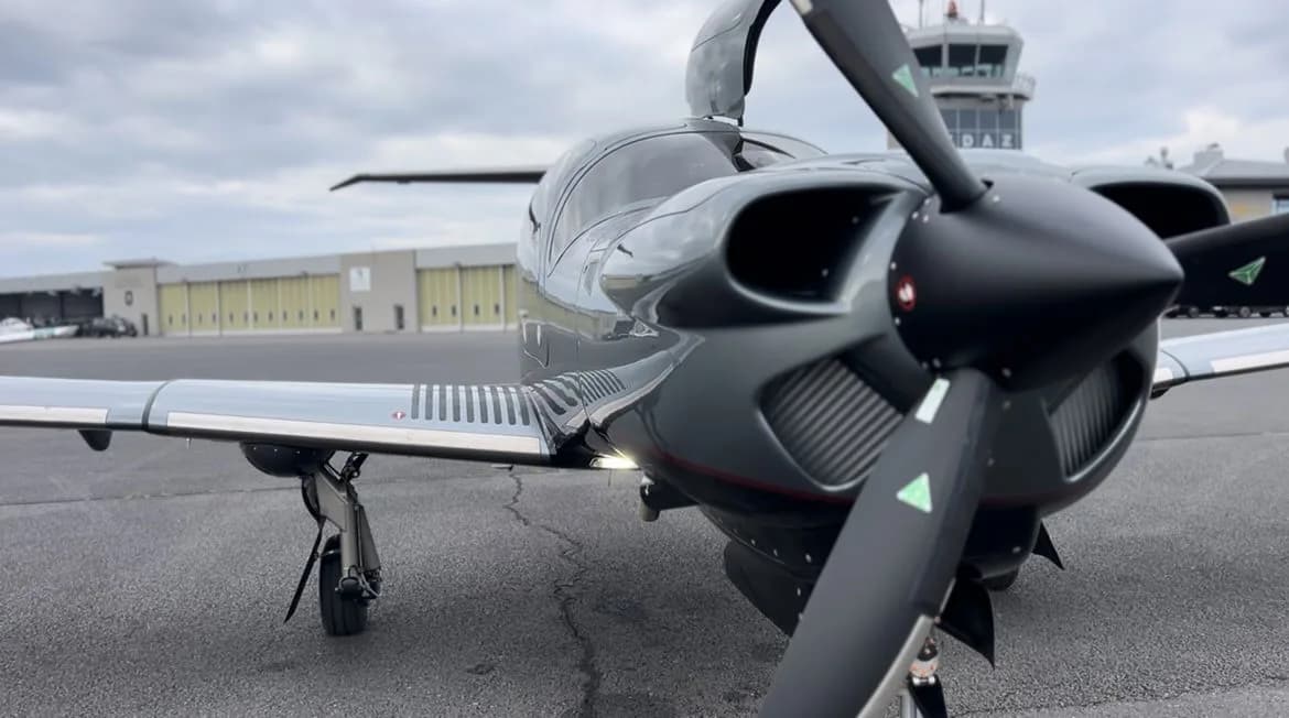 Close-up of the propeller and nose of a gray Diamond DA50 RG aircraft parked on the tarmac.