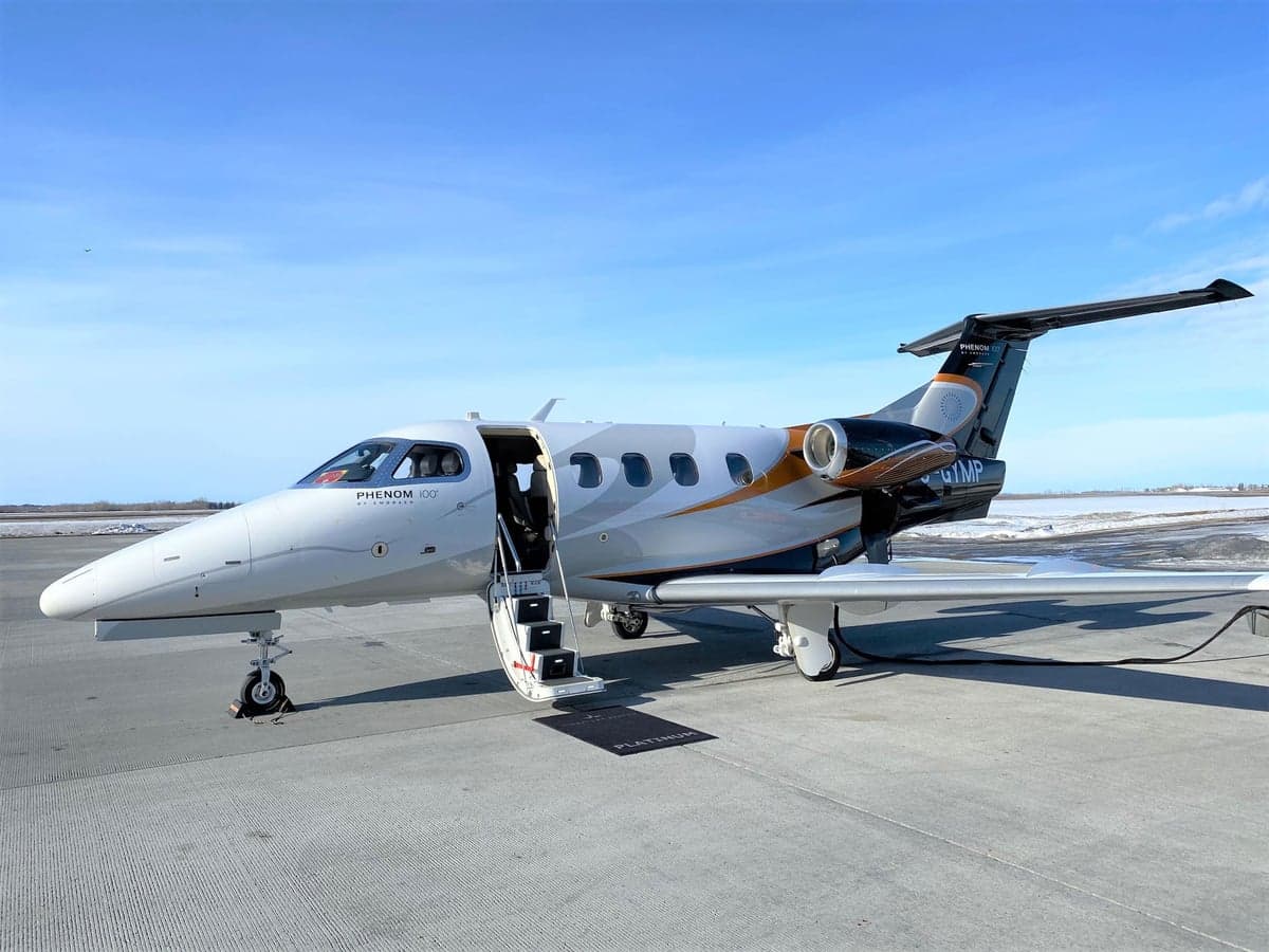 A Phenom 100EX business jet is parked on the tarmac with its door open.
