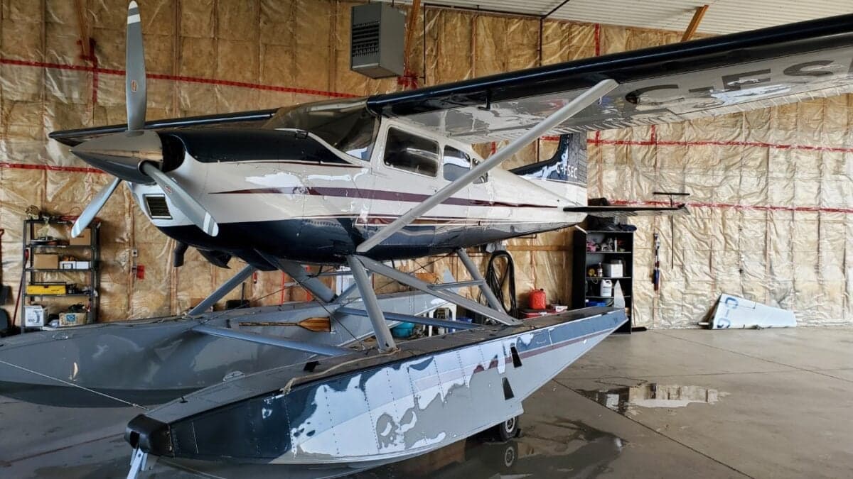 Close up side view of a white and blue Cessna on floats inside a hangar.