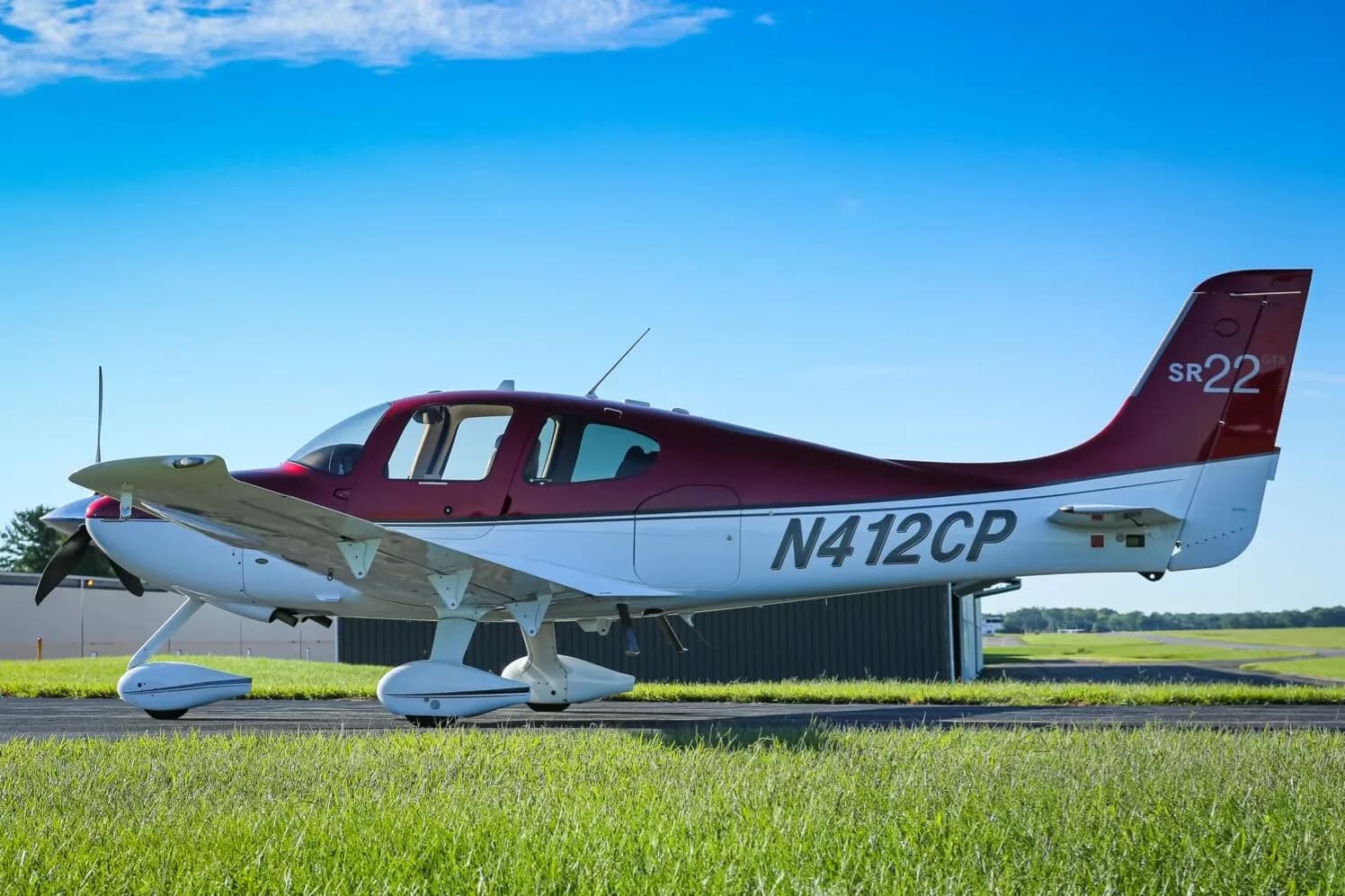 A red and white Cirrus SR22 GTS aircraft (N412CP) parked on an airfield with green grass in the foreground.