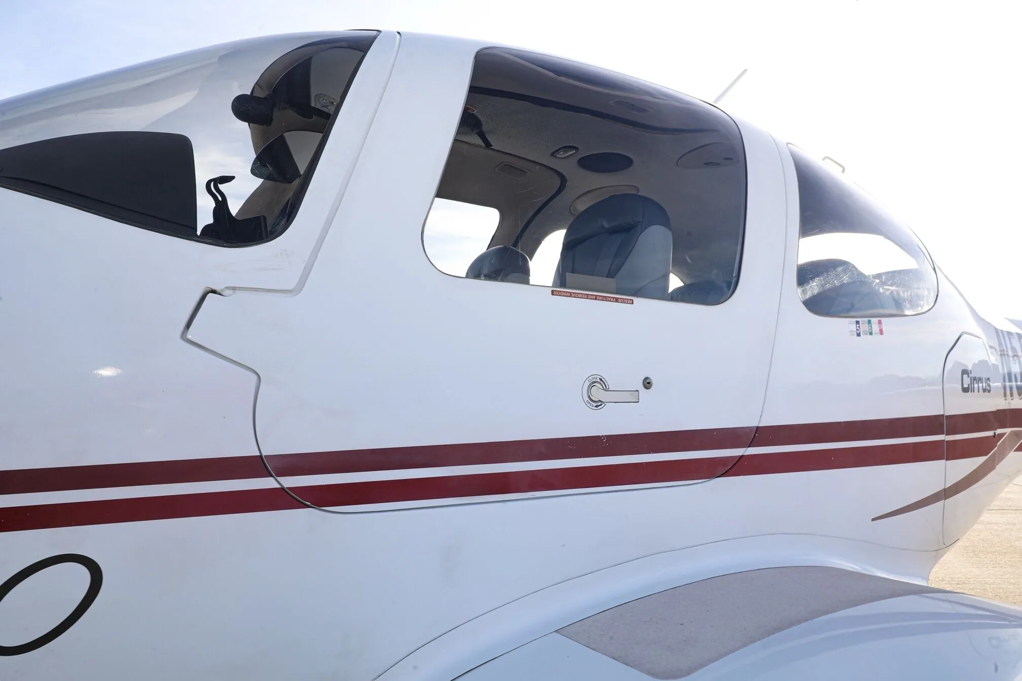 Close-up side view of the cockpit area of a white Cirrus SR20 aircraft with red stripes.