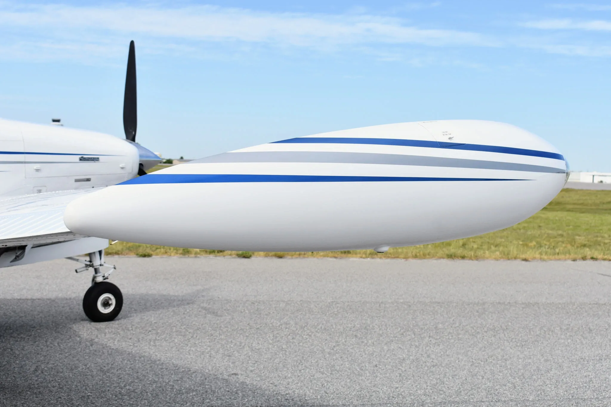 A close-up side view of the white wingtip of a Beechcraft Bonanza F33A with blue and grey stripes.