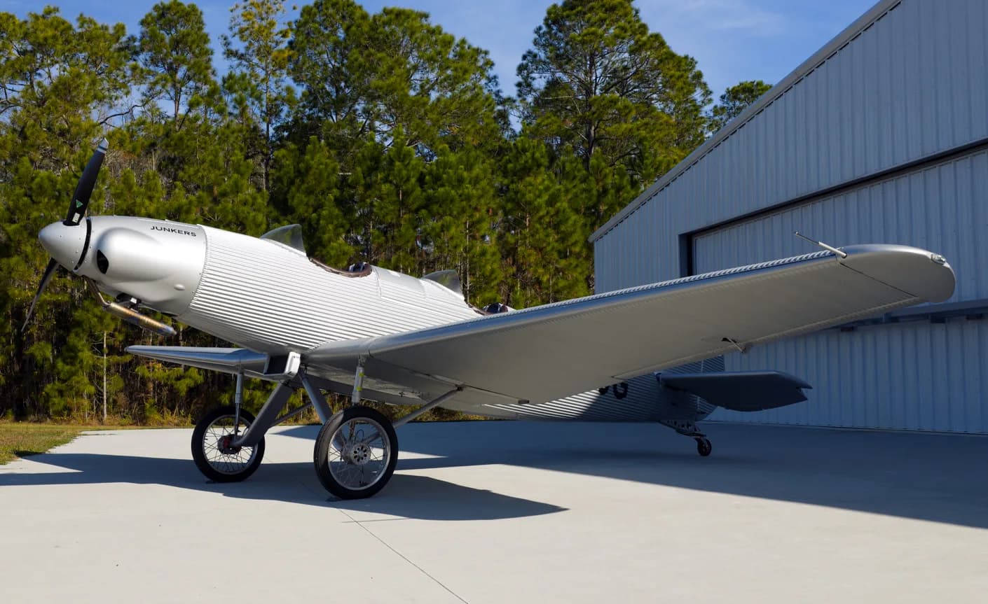 A Junkers aircraft parked outside a hangar with trees in the background.
