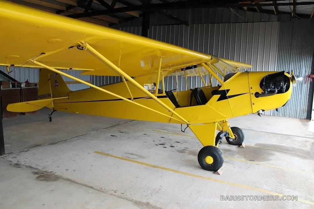A yellow single-engine aircraft with black stripes and registration N26074, parked in a hangar.